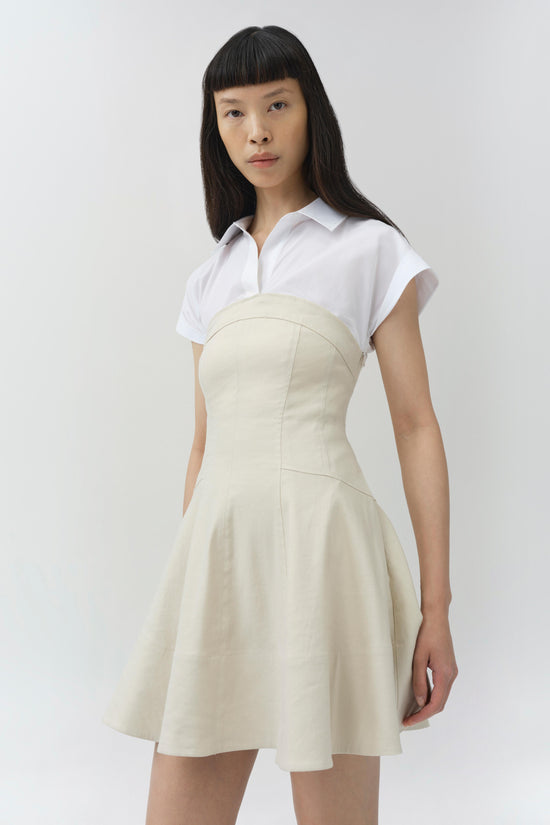 Woman wearing a white collared short-sleeve top with a cream-colored linen mini dress featuring a fitted bodice and flared sk