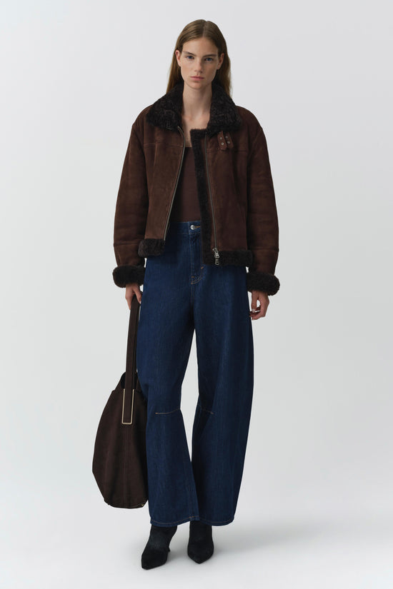 Brown suede jacket with black shearling collar and cuff trim, worn with dark jeans.