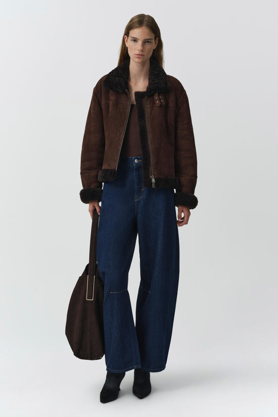 Brown suede jacket with black shearling collar and cuff trim, worn with dark jeans.