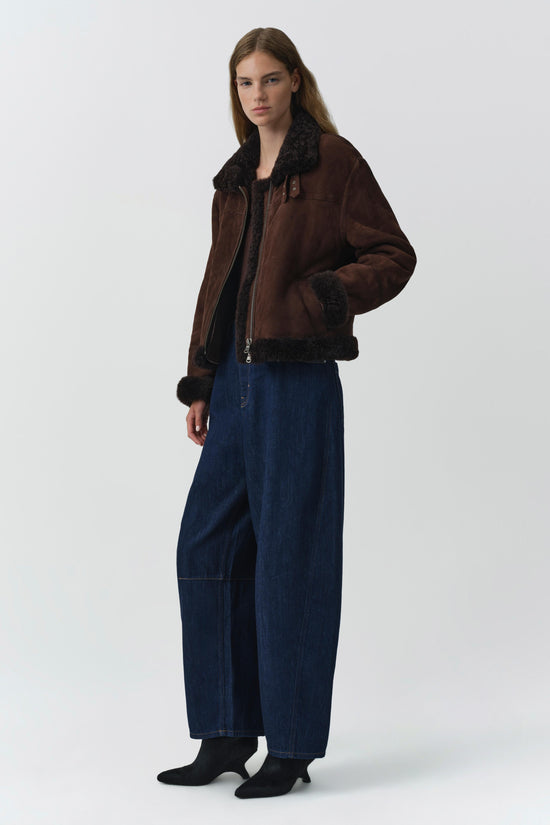 Brown suede jacket with black shearling collar, cuffs, and lining, worn with dark denim jeans.