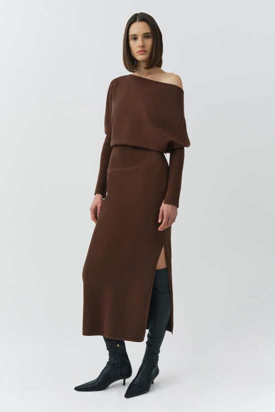Brown off-shoulder dress with long sleeves, layered top, and side slit, styled with black boots.