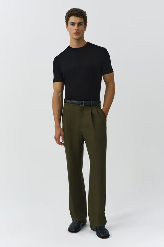 Man wearing olive green pleated trousers with a black t-shirt and dark belt.