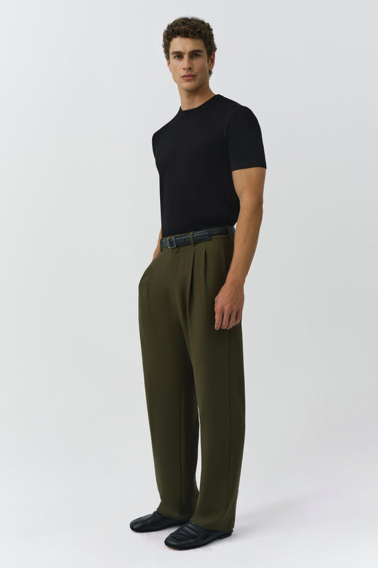 Olive green pleated trousers with front creases, worn with black t-shirt and leather belt.