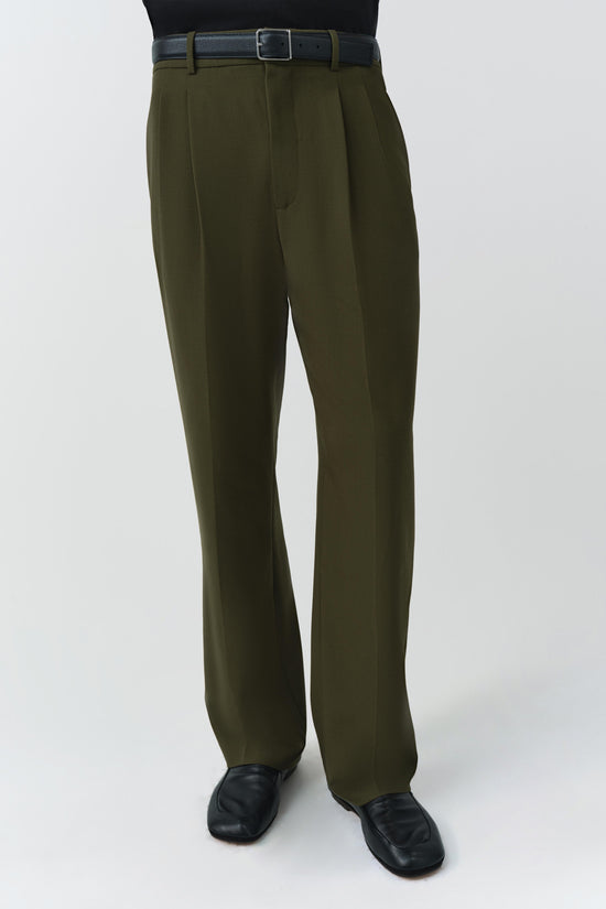Olive-green pleated trousers with gray fabric belt worn with black leather loafers.