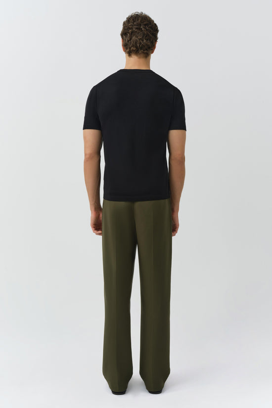 Olive green pleated trouser with high waist, worn with black short-sleeve t-shirt, rear view.
