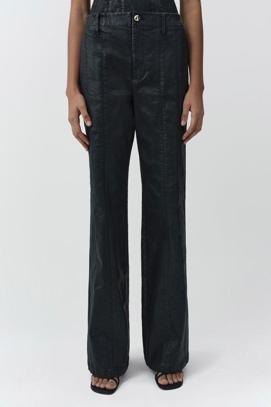 Dark coated denim trousers with straight legs and high waist, worn with black slide sandals.