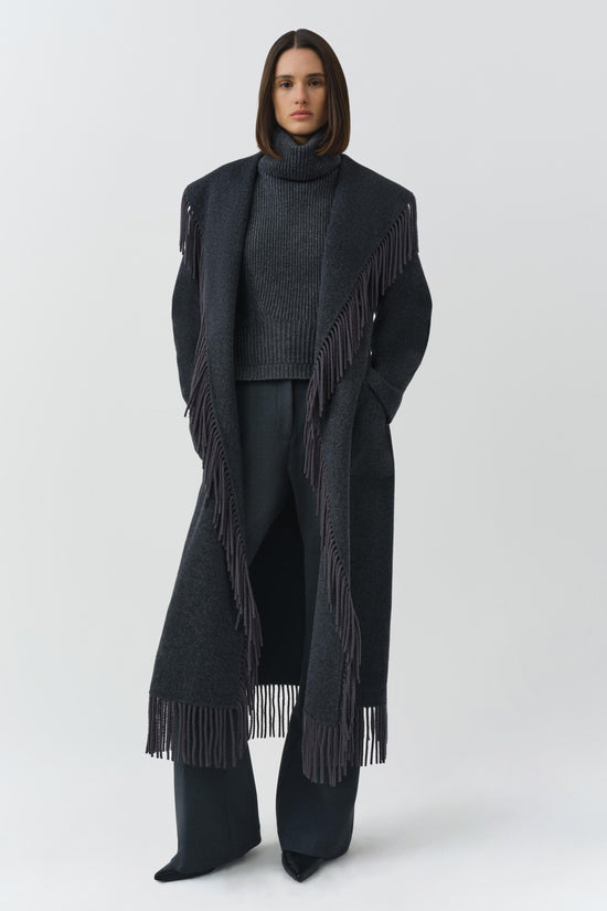 Charcoal wool coat with fringe trim on front edges and hem, worn open over a gray turtleneck.