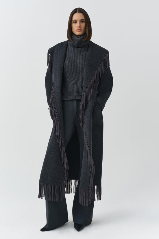 Charcoal wool coat with fringe trim on front edges and hem, worn open over a gray turtleneck.