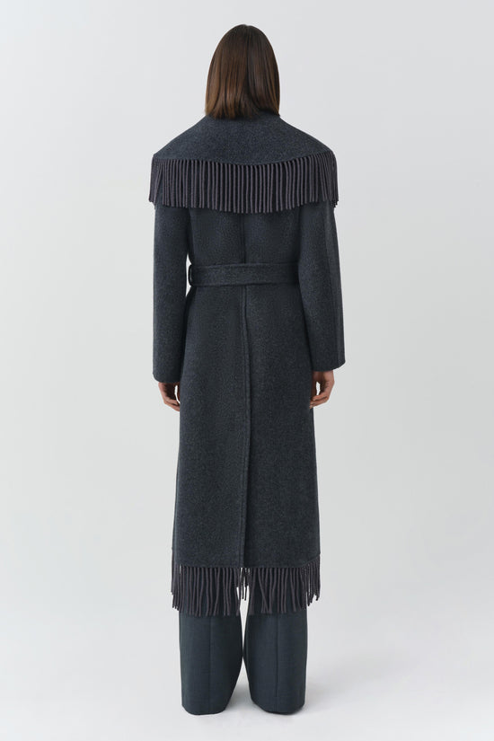 Charcoal wool coat with pleated fringe details on shoulders and hem, belted waist, long sleeves, worn over black pants.