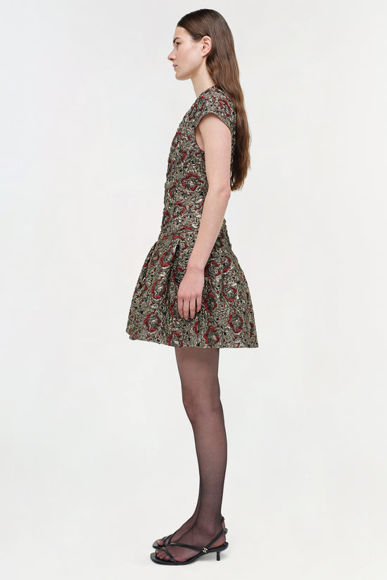 Sleeveless mini dress with red and gold jacquard pattern, fitted bodice, and flared skirt, worn with tights and black heels.