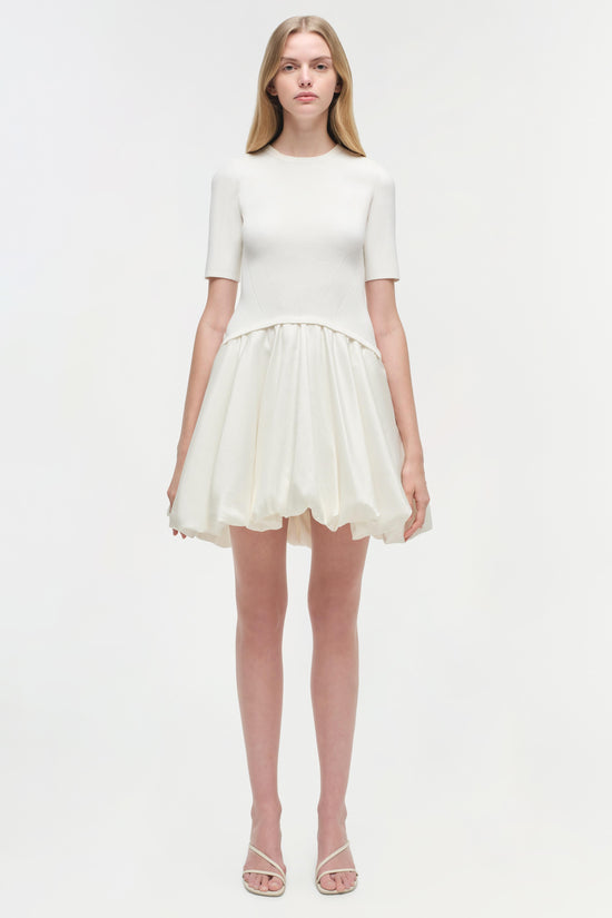 Cream mini dress with ribbed short-sleeve top and pleated skirt bottom on model.
