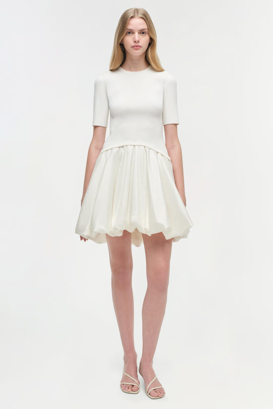 White mini dress with ribbed knit top and pleated skirt, shown on model wearing white sandals.