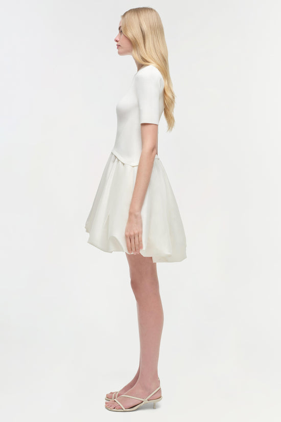 White mini dress with ribbed short-sleeve top and flowing skirt, shown on model in side profile view.