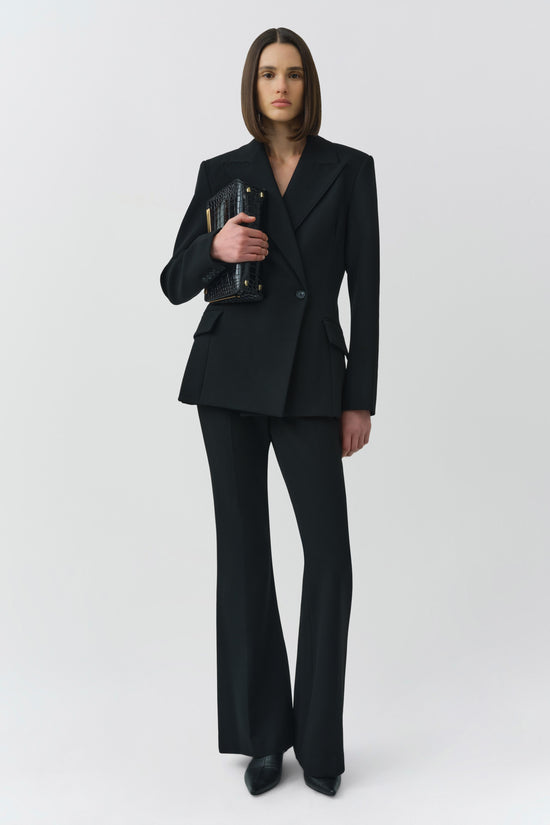 Black double-breasted blazer with notch lapels paired with matching flared trousers, worn with a black clutch.