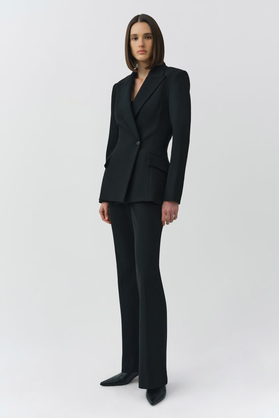 Woman wearing black tailored blazer with notch lapels and matching flared trousers.