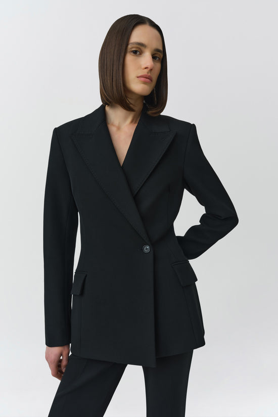 Black double-breasted blazer with notch lapels, fitted waist, and button closure worn with matching trousers.