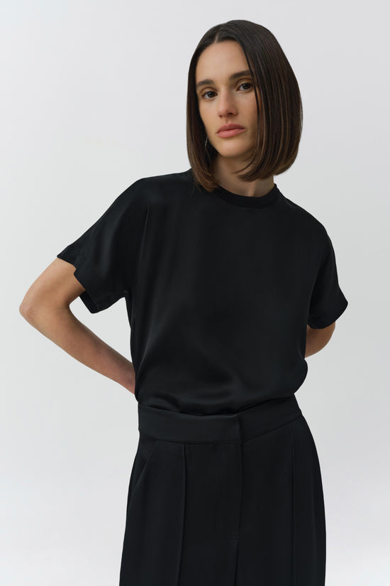 Black crewneck t-shirt with short sleeves, worn by a person against a white background.