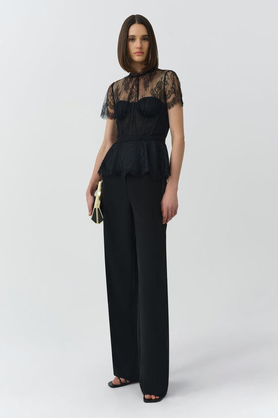 Black lace bustier top with sheer patterned sleeves and structured bodice worn with wide-leg trousers.