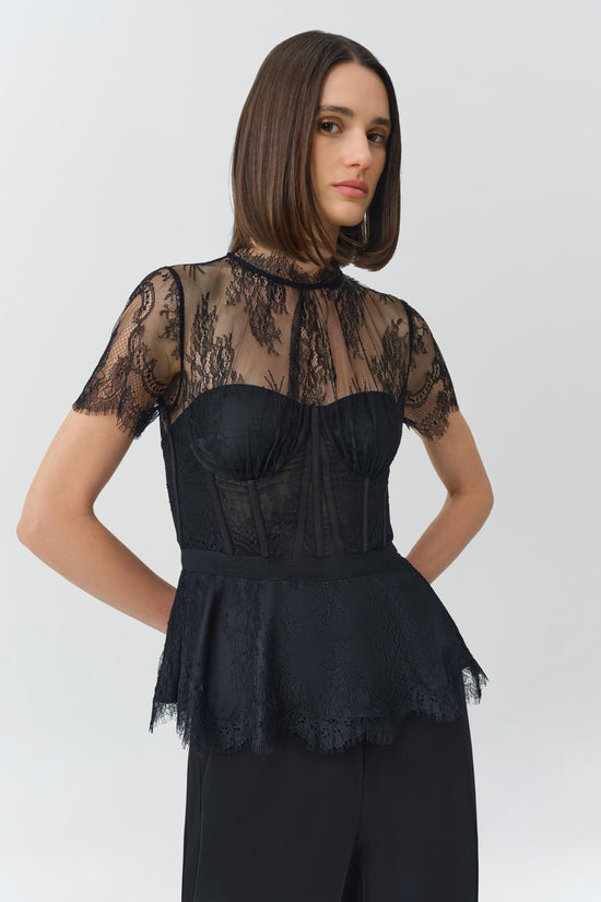 Black lace bustier top with sheer lace sleeves and structured corset bodice worn with high-waisted trousers.