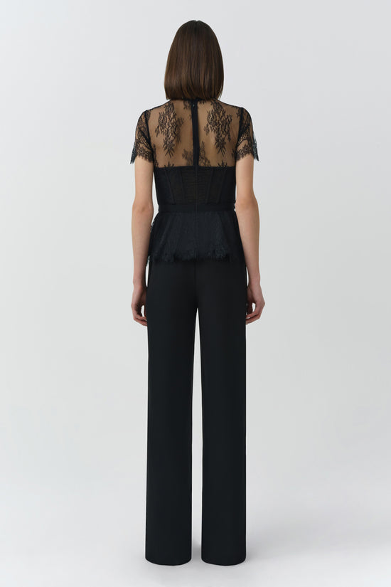 Black lace bustier top with short sleeves and sheer patterned back, worn with high-waisted wide-leg trousers.