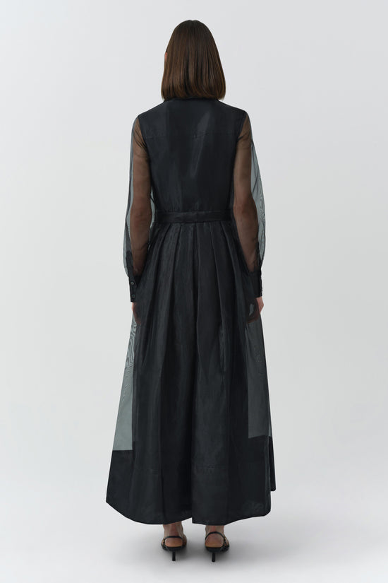 Black sleeveless dress with sheer long sleeves and pleated skirt, shown from back view on model.