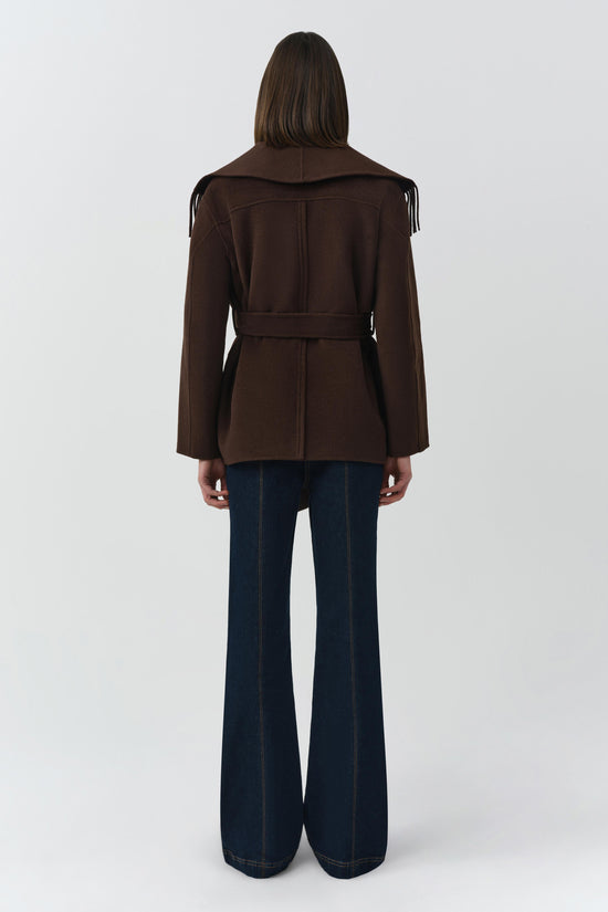 Brown wool jacket with fringe trim on shoulders and belt at waist, worn with dark denim flare pants.