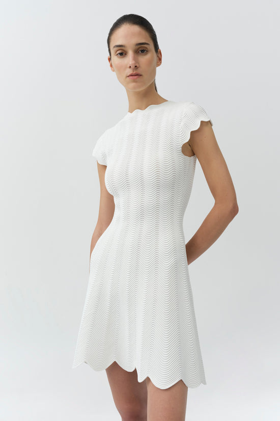 White wavy knit mini dress with scalloped edges and short cap sleeves on a model.