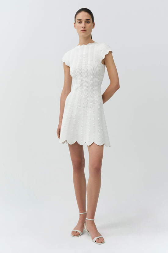 White wavy knit mini dress with scalloped hem and short sleeves on a model.