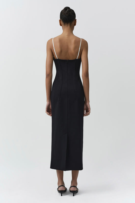 Woman wearing black midi dress with thin white straps and open back, styled with black heeled sandals.