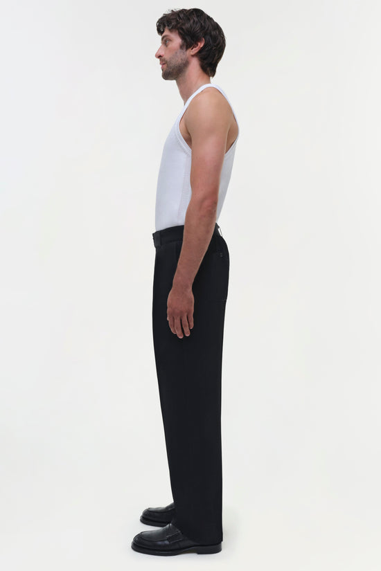 Black straight-leg trousers with high waist on model wearing white tank top, side view.