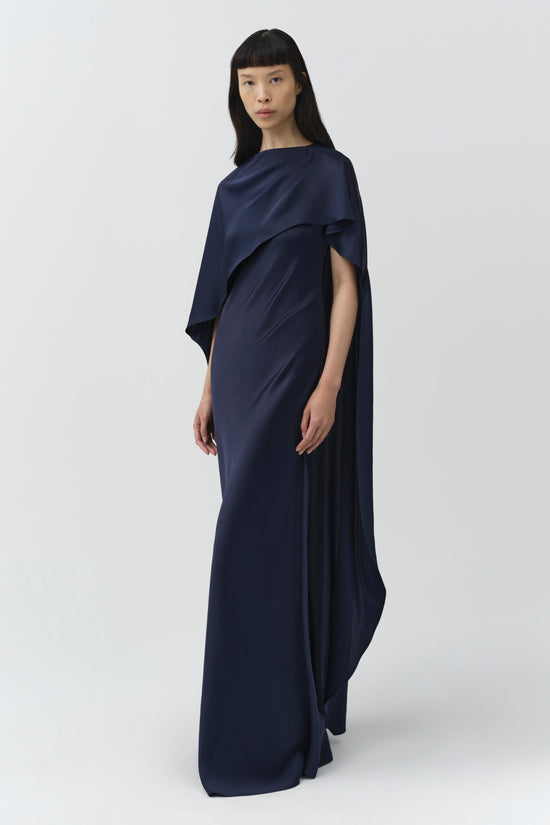 Woman wearing navy satin gown with draped cape overlay extending to floor.