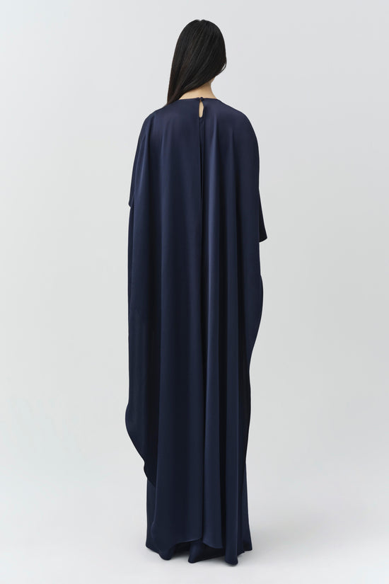 Woman wearing a navy satin cape gown with flowing fabric and back keyhole detail.