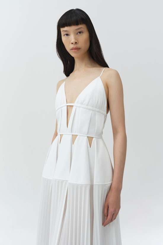 White cotton gown with pleated skirt, deep V-neckline, and cutout details at waist and bodice.