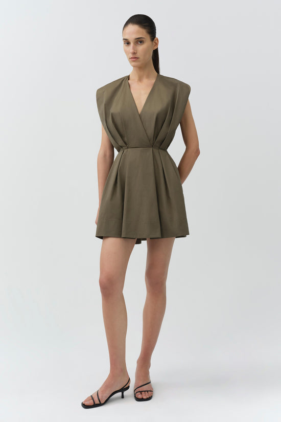 Olive-green cotton cape mini dress with wrap front, cinched waist, and short sleeves worn with black strappy sandals.