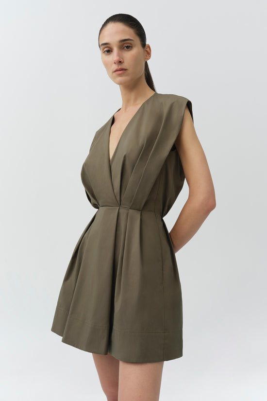Olive green cotton cape mini dress with V-neckline, sleeveless design, and belted waist worn by model against neutral backgro