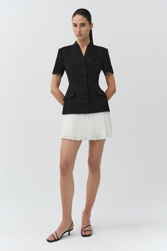 Black short-sleeve blazer with button front and patch pockets paired with white pleated mini skirt.