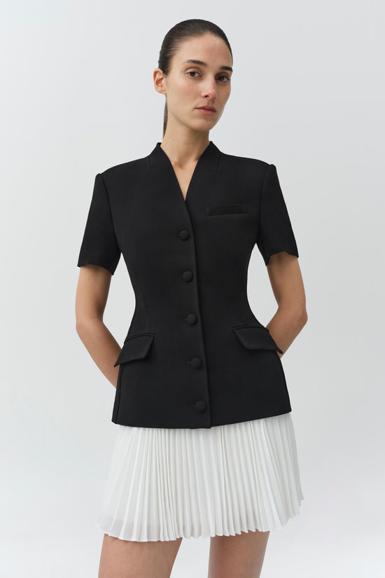 Black blazer mini dress with short sleeves, button front, chest pocket, and white pleated skirt bottom.