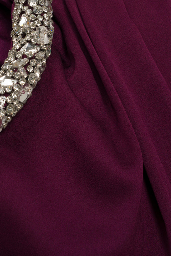 Burgundy satin gown detail showing jeweled embellishment along the neckline and draped fabric.