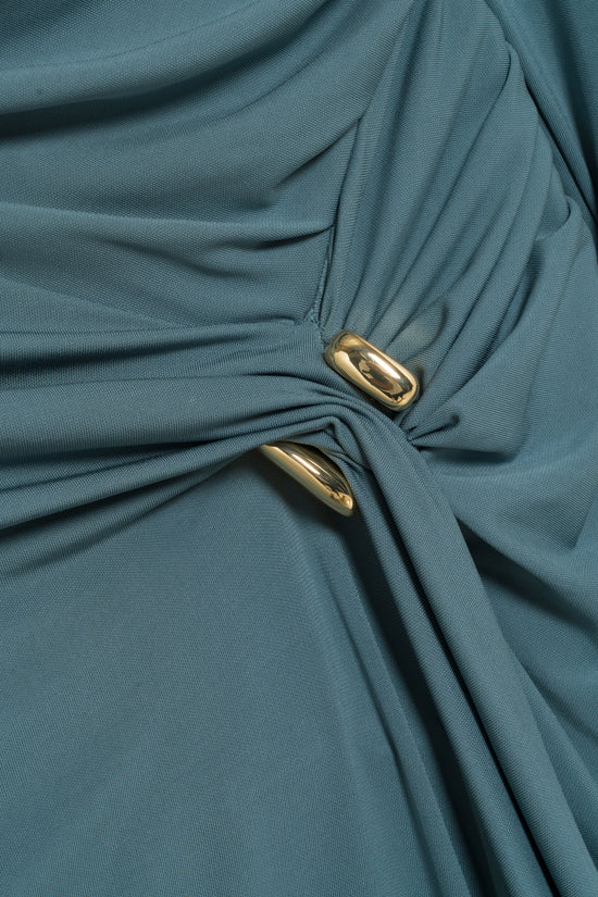 Slate blue jersey gown with draped fabric and gold oval embellishments at the waist.