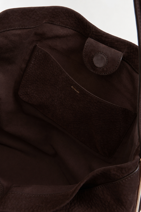 Dark brown nubuck leather bucket bag with rounded silhouette, snap closure, and interior pocket visible.