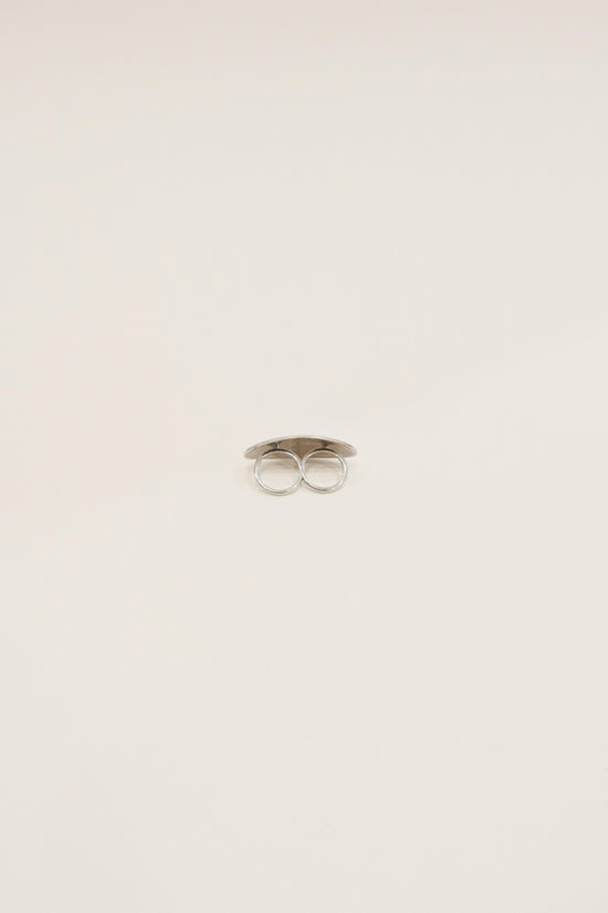 Silver-toned double ring with two circular loops connected by a flat band, displayed against a neutral background.