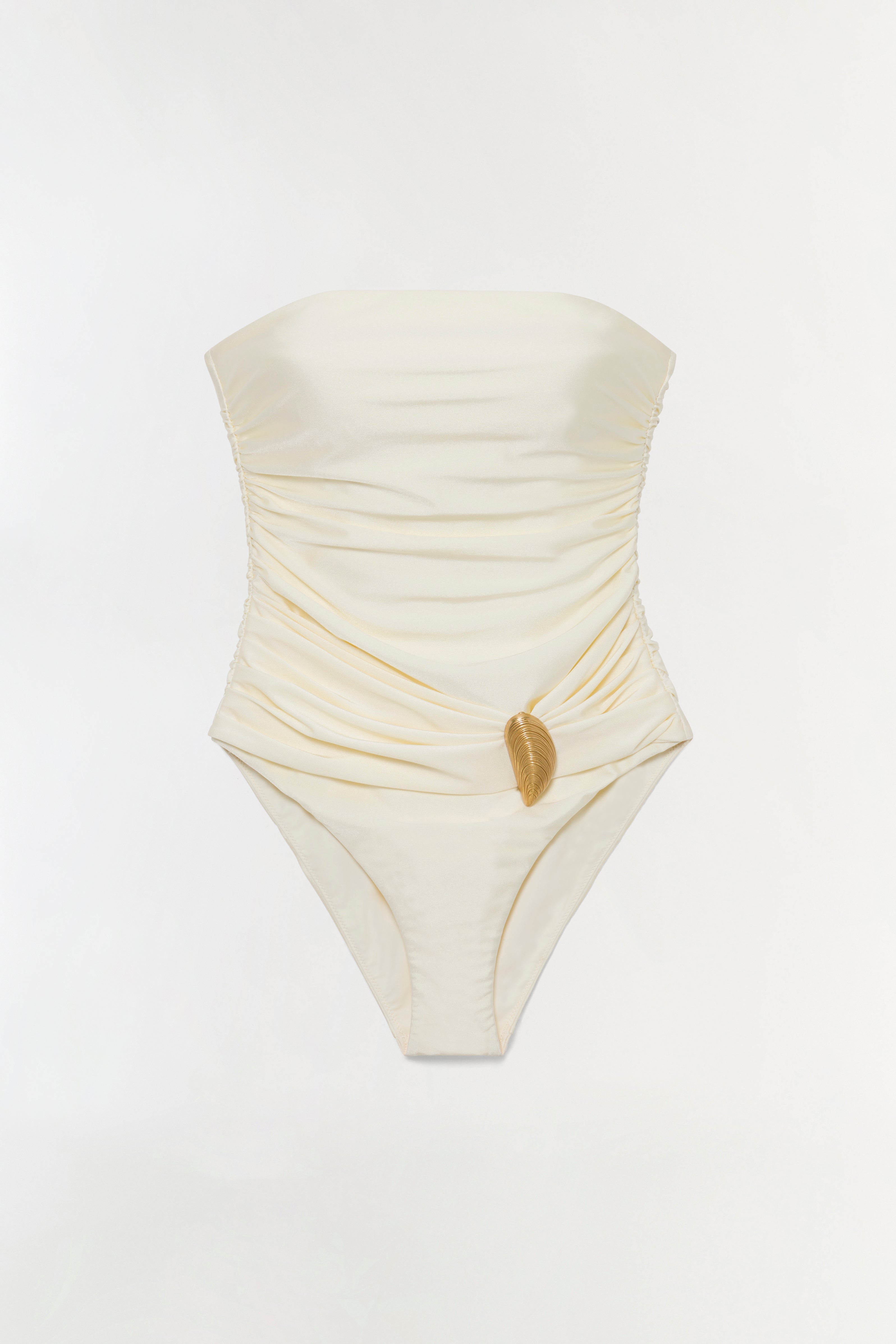 Cream strapless one-piece swimsuit with ruched detailing and a gold shell charm at the waist.