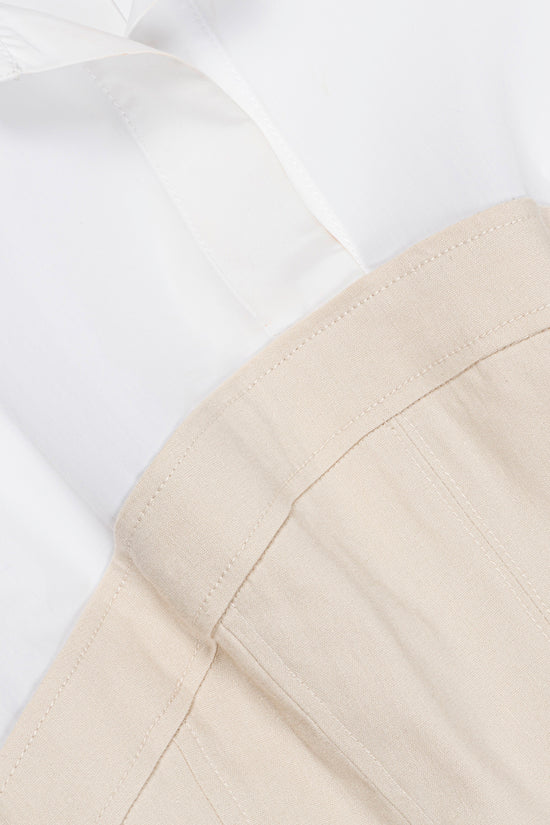 White linen mini dress with beige underlay, showing seam details and draped fabric.