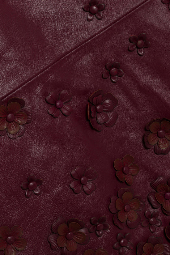 Burgundy leather fabric with embossed floral appliqués in varying sizes scattered across the surface.