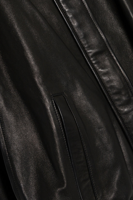 Black leather cape jacket with draped fabric and vertical seam detail.