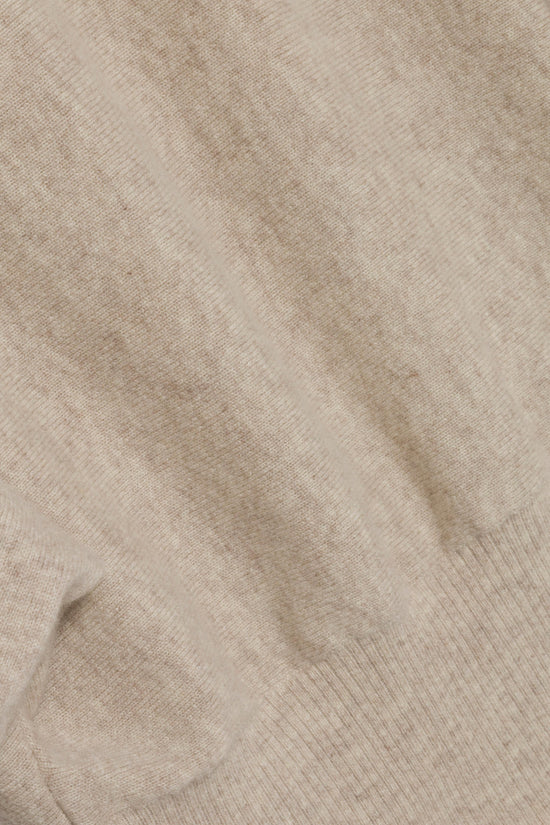 Beige cashmere knit fabric with ribbed texture visible at cuff and hem.