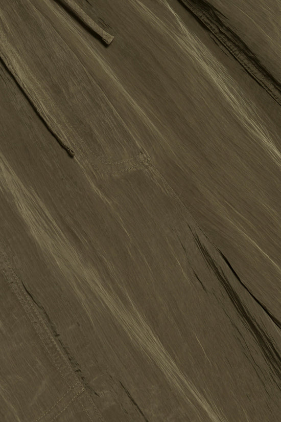 Olive-toned parachute pant fabric with visible seams and pocket details, shot at an angle.