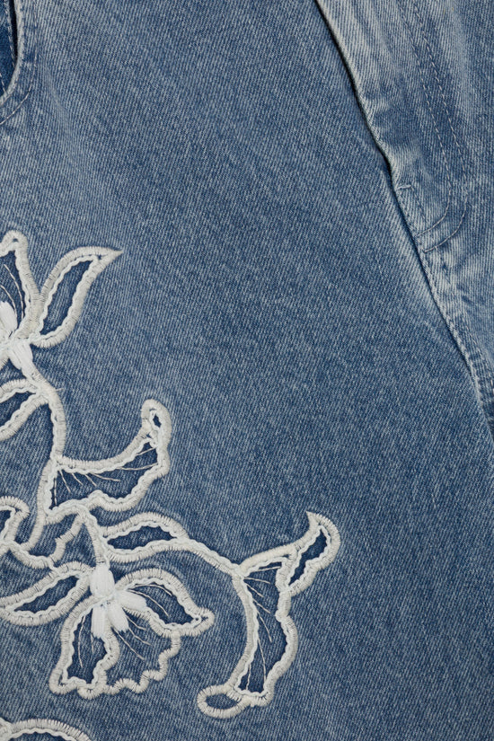 Blue denim fabric with white embroidered ornamental design detail on leg.