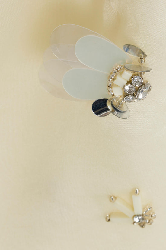 Cream organza fabric with gold-toned brooch and rhinestone embellishments displayed on beige surface.