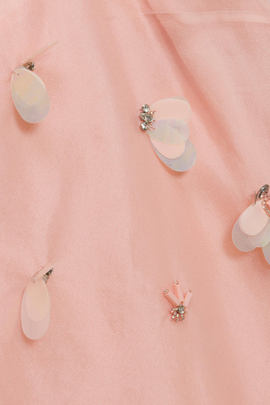 Pink organza fabric with iridescent petal-shaped embellishments and rhinestone clusters scattered across surface.